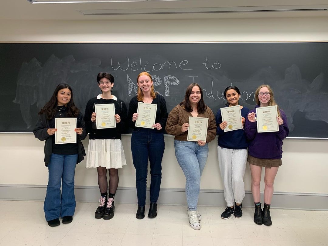 Induction from the University of Virginia chapter, 5 newly inducted students are smiling and standing in front of a chalkboard that reads” Welcome to the NRP induction” and holding their certificates.
