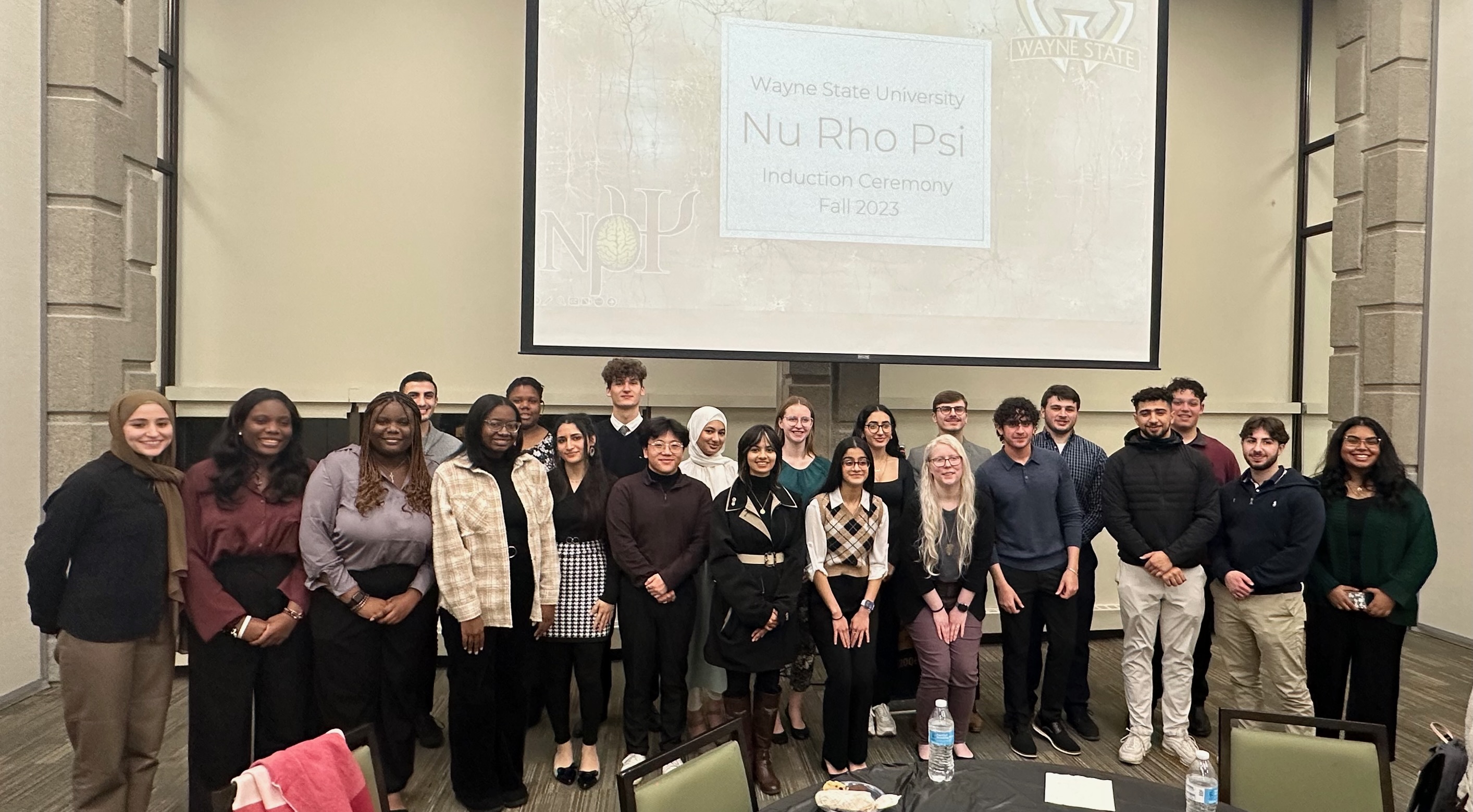 Induction from Wayne State University with all of the newly inducted members. Above them is a slide that reads “Wayne State Nu Rho Psi Induction Ceremony Fall 2023”. There are 22 members total in two different rows.