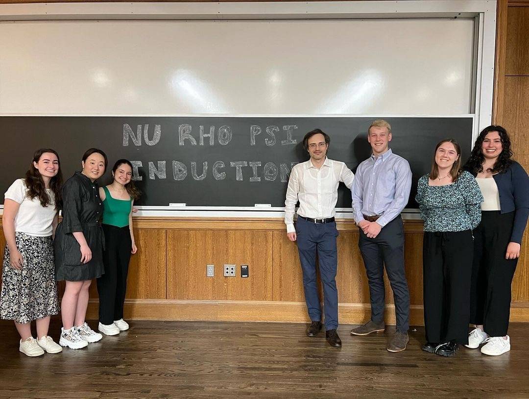 Boston College Spring 2024 induction ceremony. There are 6 students and their guest speaker, Dr. Stefano Anzellotti of the BC Psychology department, standing in front of a chalkboard that reads “Nu Rho Psi induction”. Three students are on the left of the chalkboard, and three students are on the right of the chalkboard, with Dr. Anzellotti standing in the centermost spot on the right side.