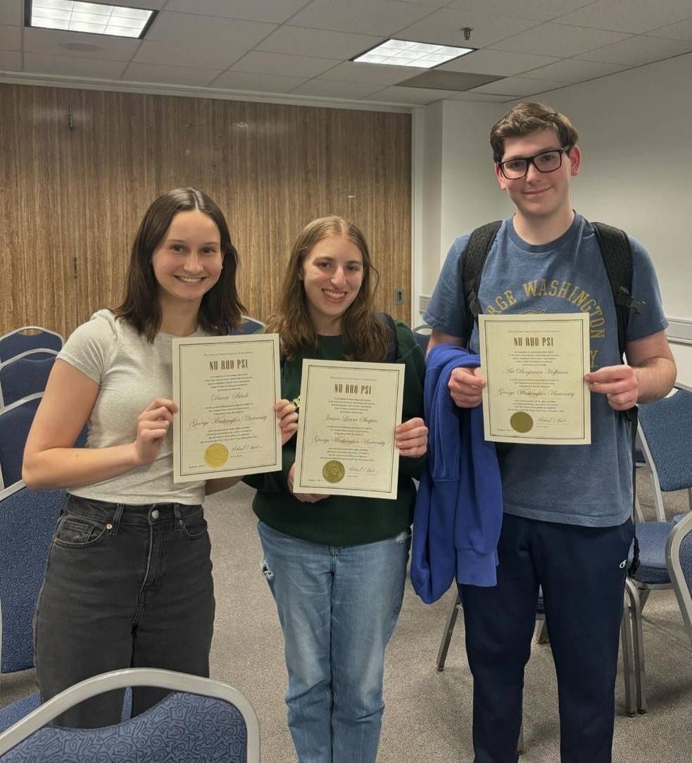 Three newly inducted George Washington University students holding their certificates and smiling.